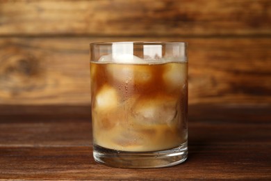 Photo of Glass of coffee with milk and ice cubes on wooden table