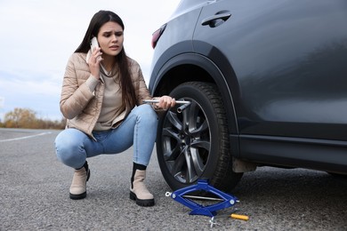 Photo of Worried young woman calling car service. Tire puncture