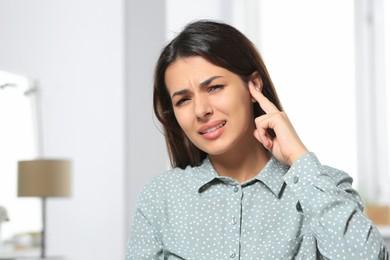 Photo of Young woman suffering from ear pain indoors