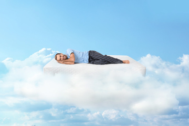 Image of Young man lying on mattress in clouds