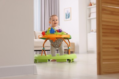 Photo of Cute little boy making first steps with baby walker at home