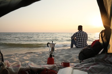 Photo of Man enjoying sunset on beach, view from camping tent