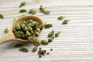 Photo of Spoon with dry cardamom pods on white wooden table, space for text