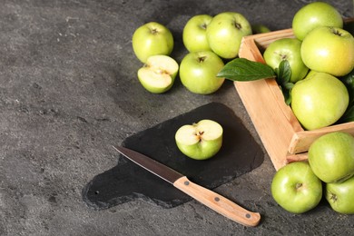 Photo of Ripe green apples, cutting board and knife on grey table. Space for text