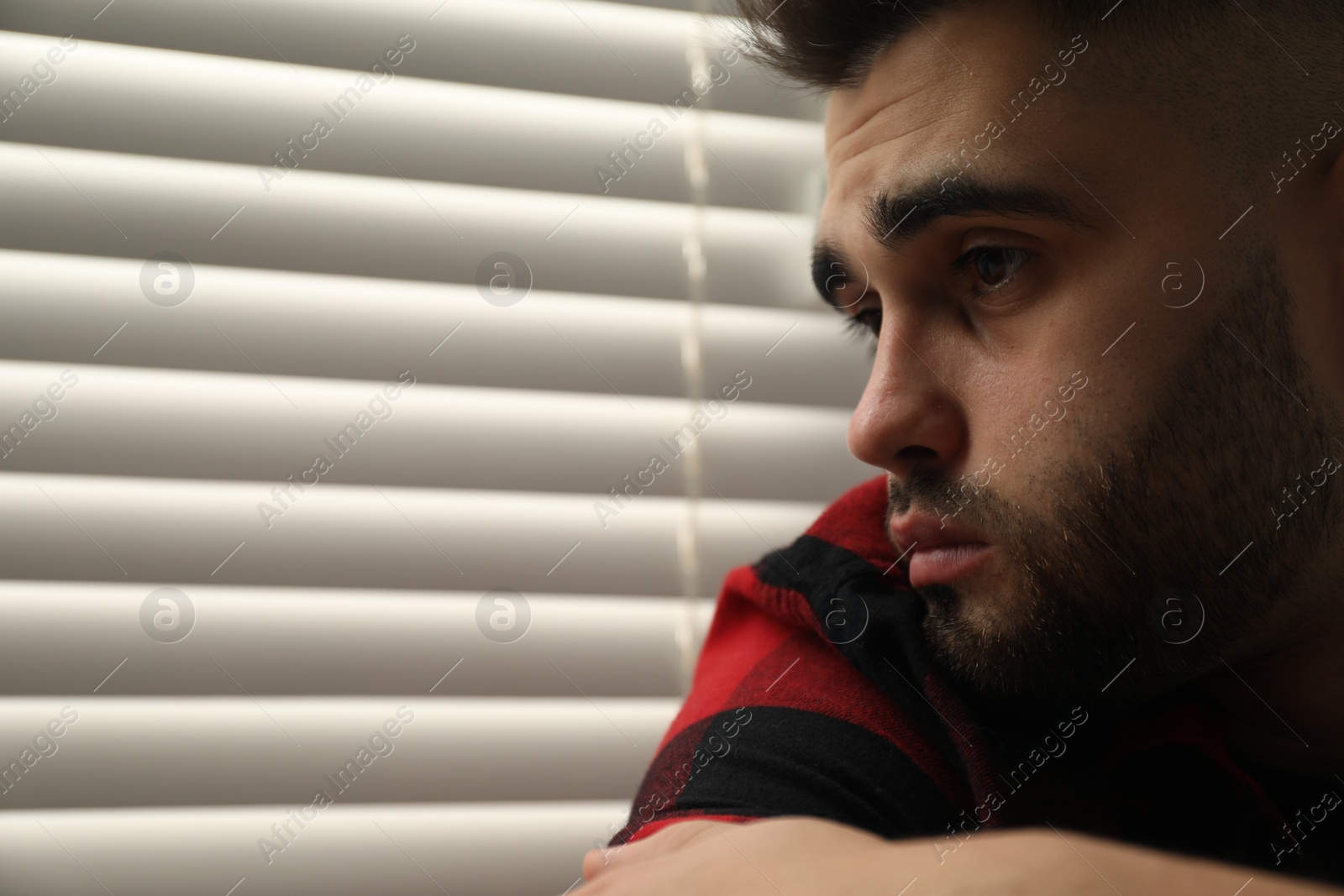 Photo of Sad young man near closed blinds at home. Space for text