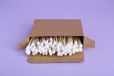 Box with wooden cotton buds on violet background