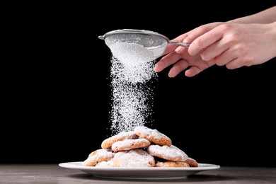 Woman with sieve sprinkling powdered sugar onto cookies at grey table, closeup