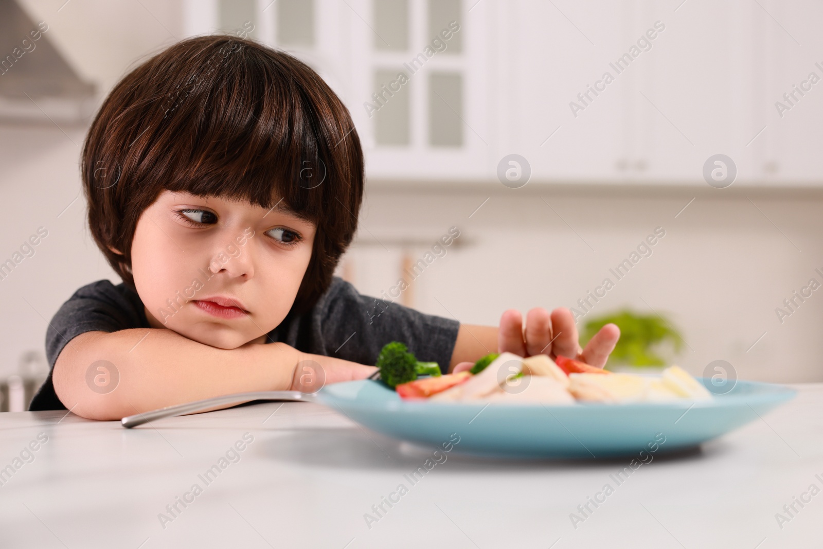 Photo of Cute little boy refusing to eat dinner in kitchen