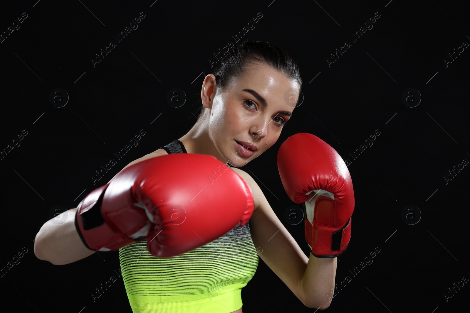 Photo of Beautiful woman in boxing gloves training on black background