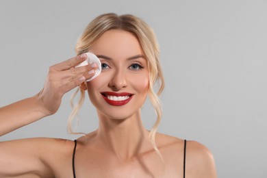 Photo of Smiling woman removing makeup with cotton pad on light grey background. Space for text