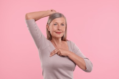 Photo of Beautiful senior woman doing breast self-examination on pink background