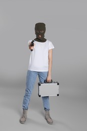 Woman wearing knitted balaclava with metal briefcase gun on grey background