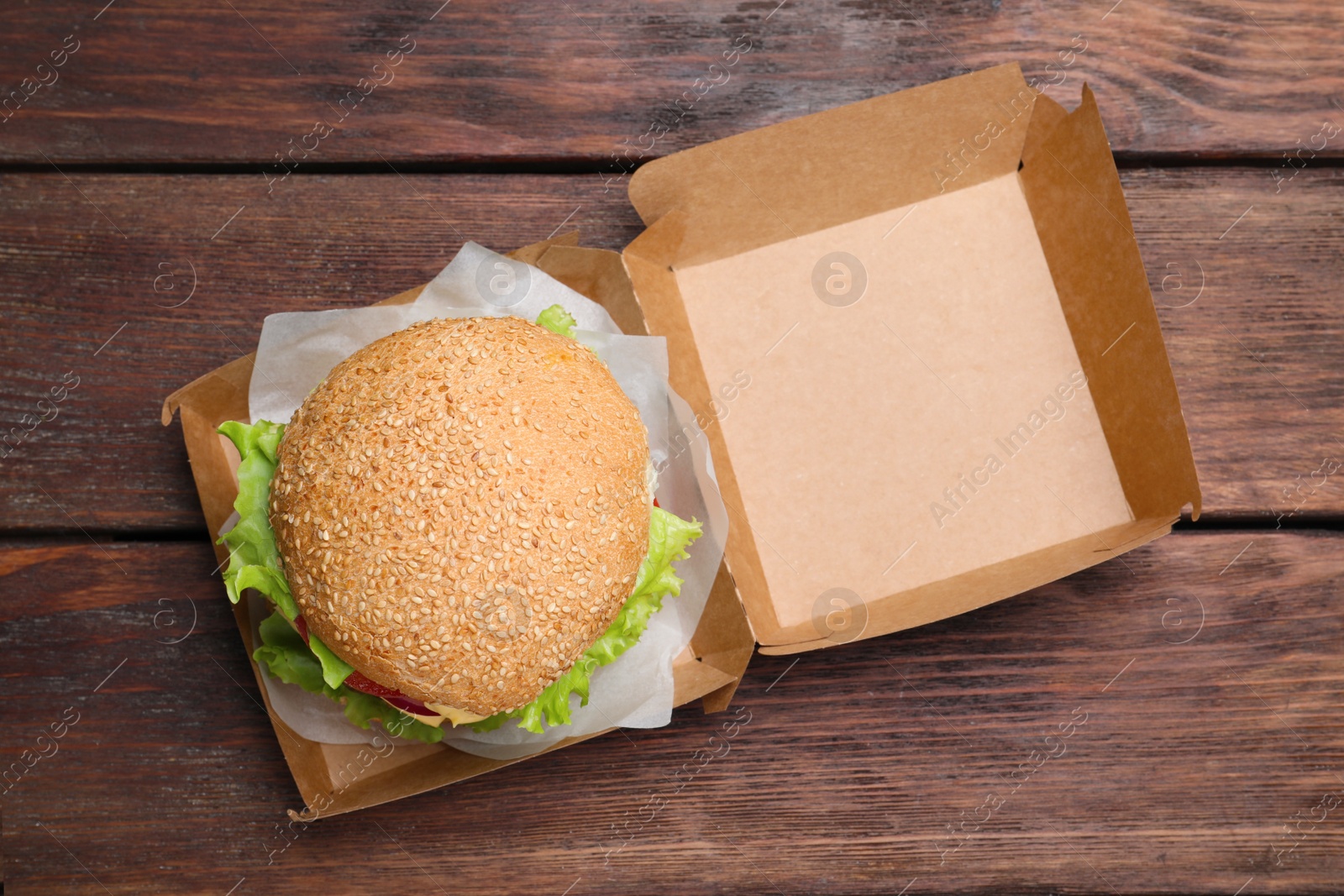 Photo of Delicious burger in cardboard box on wooden table, top view