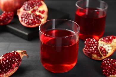 Photo of Tasty pomegranate juice in glasses and fresh fruits on black wooden table, closeup