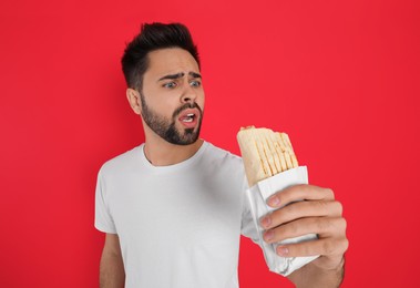 Photo of Emotional young man holding tasty shawarma on red background