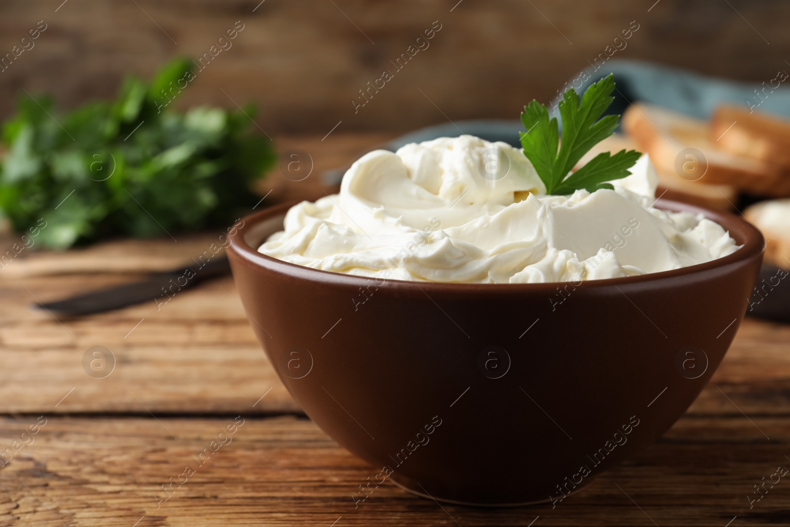 Photo of Bowl of tasty cream cheese and parsley on wooden table, closeup