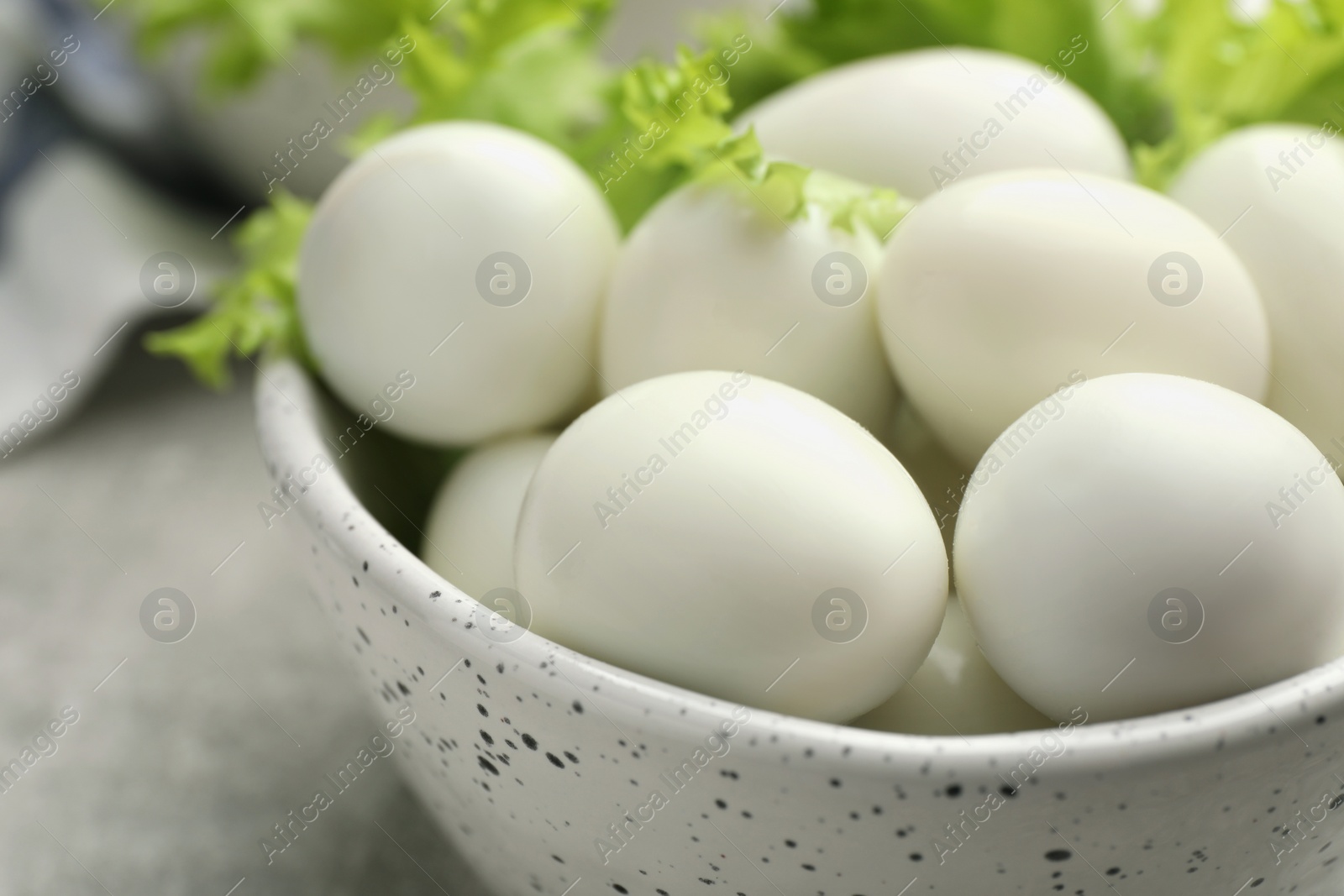 Photo of Peeled boiled quail eggs in bowl on grey table, closeup