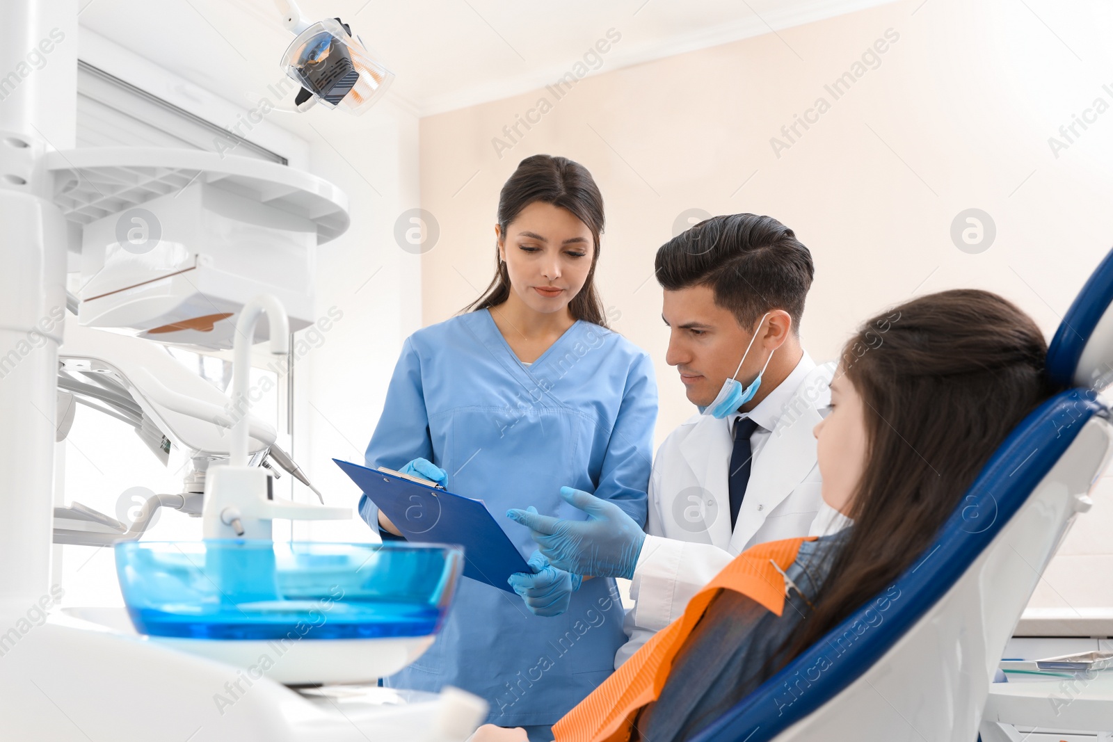 Photo of Professional dentist and assistant working with little girl in clinic