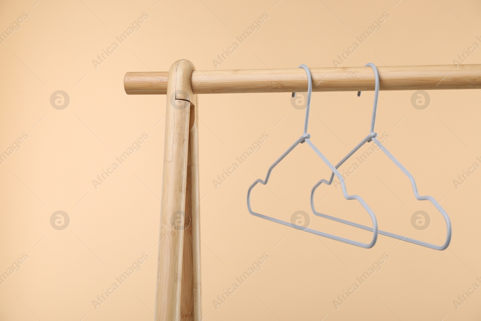 Photo of Empty clothes hangers on wooden rack against beige background