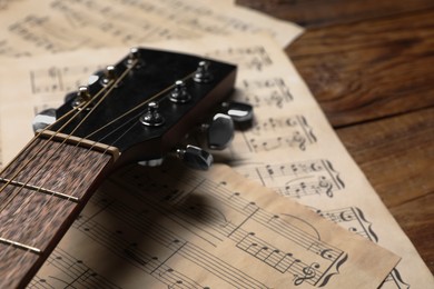 Photo of Paper sheets with music notes and guitar neck on wooden table, closeup