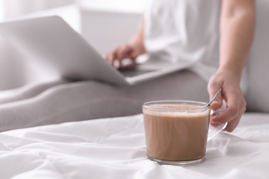 Photo of Woman taking cup of morning coffee while working on laptop in bedroom, closeup