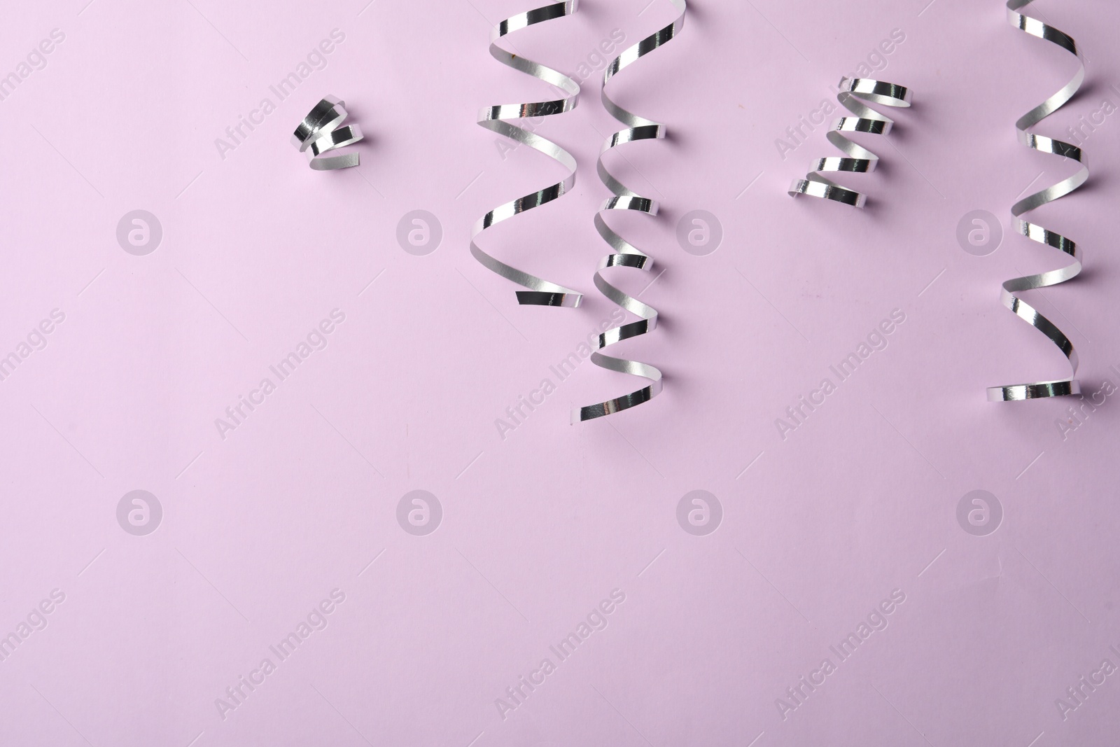 Photo of Shiny silver serpentine streamers on pink background, flat lay. Space for text