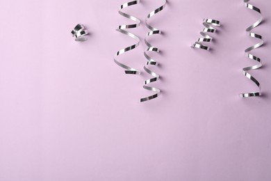 Shiny silver serpentine streamers on pink background, flat lay. Space for text