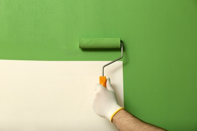 Photo of Man applying green paint with roller brush on white wall, closeup