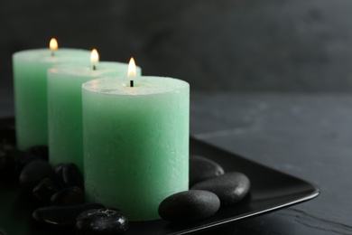 Photo of Dark plate with three burning candles and rocks on table, space for text