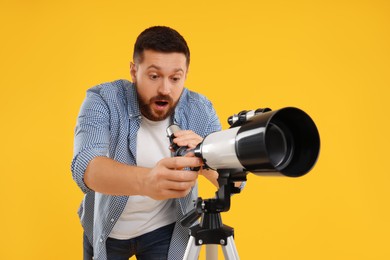 Photo of Surprised astronomer with telescope on orange background