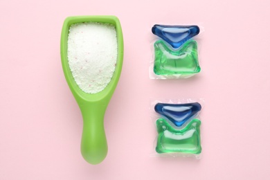 Photo of Laundry capsules and measuring scoop of washing powder on pink background, flat lay