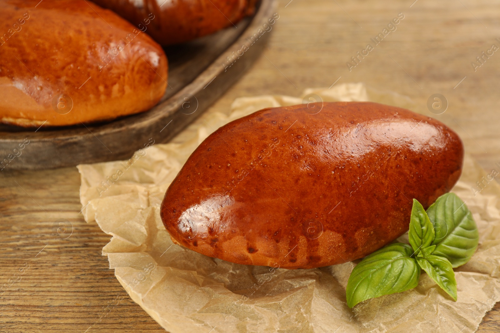 Photo of Delicious baked pirozhki and basil on wooden table, closeup