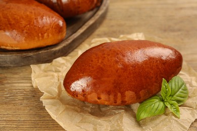 Photo of Delicious baked pirozhki and basil on wooden table, closeup