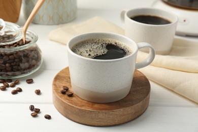 Photo of Aromatic coffee in cup and beans on white wooden table