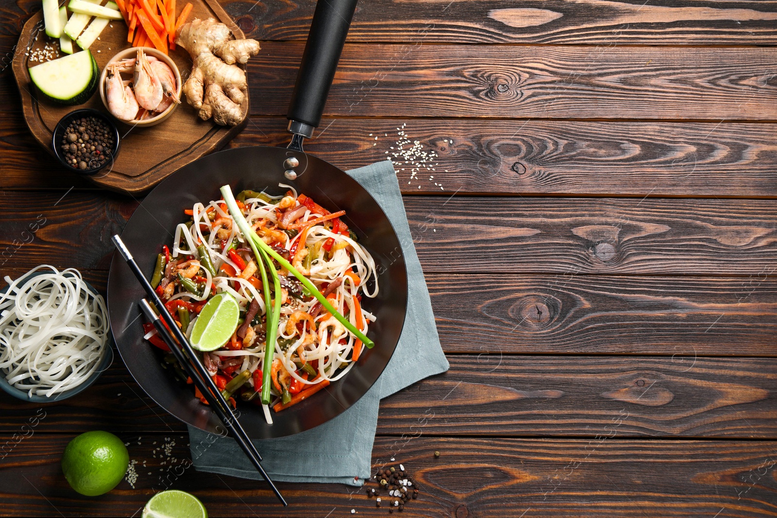 Photo of Shrimp stir fry with noodles and vegetables in wok on wooden table, flat lay. Space for text