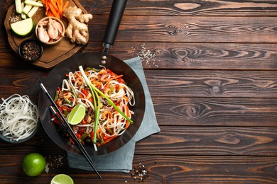 Photo of Shrimp stir fry with noodles and vegetables in wok on wooden table, flat lay. Space for text