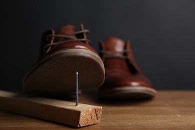 Metal nail in wooden plank and shoes on table, closeup