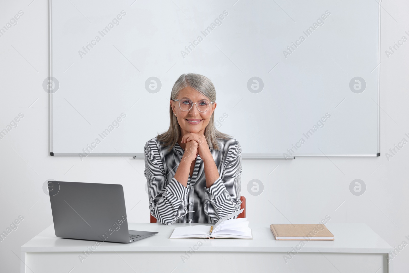 Photo of Happy professor sitting near laptop at desk in classroom, space for text