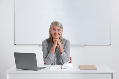 Happy professor sitting near laptop at desk in classroom, space for text