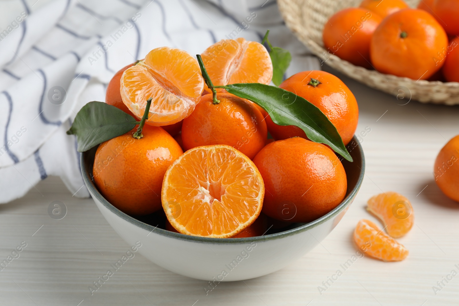 Photo of Delicious tangerines with green leaves in bowl on white wooden table, closeup