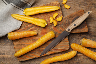 Photo of Raw yellow carrots, cutting board and knife on wooden table, flat lay