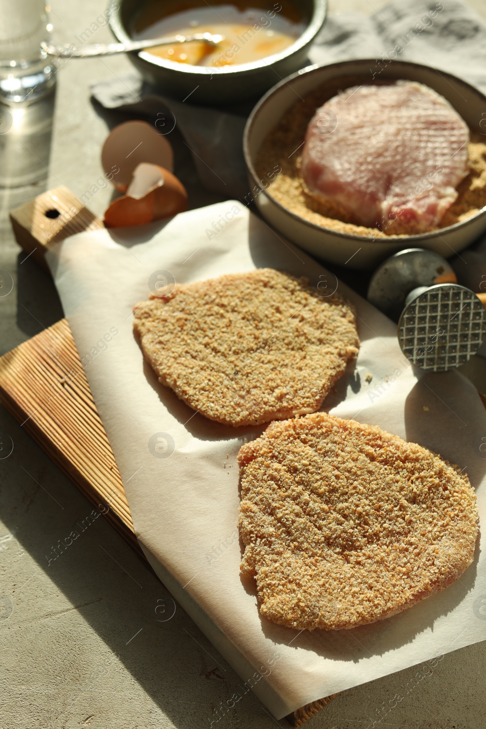 Photo of Cooking schnitzel. Raw pork chops in bread crumbs, meat mallet and ingredients on grey table