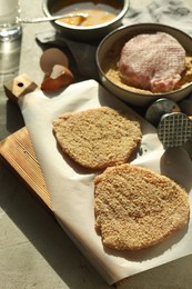Photo of Cooking schnitzel. Raw pork chops in bread crumbs, meat mallet and ingredients on grey table