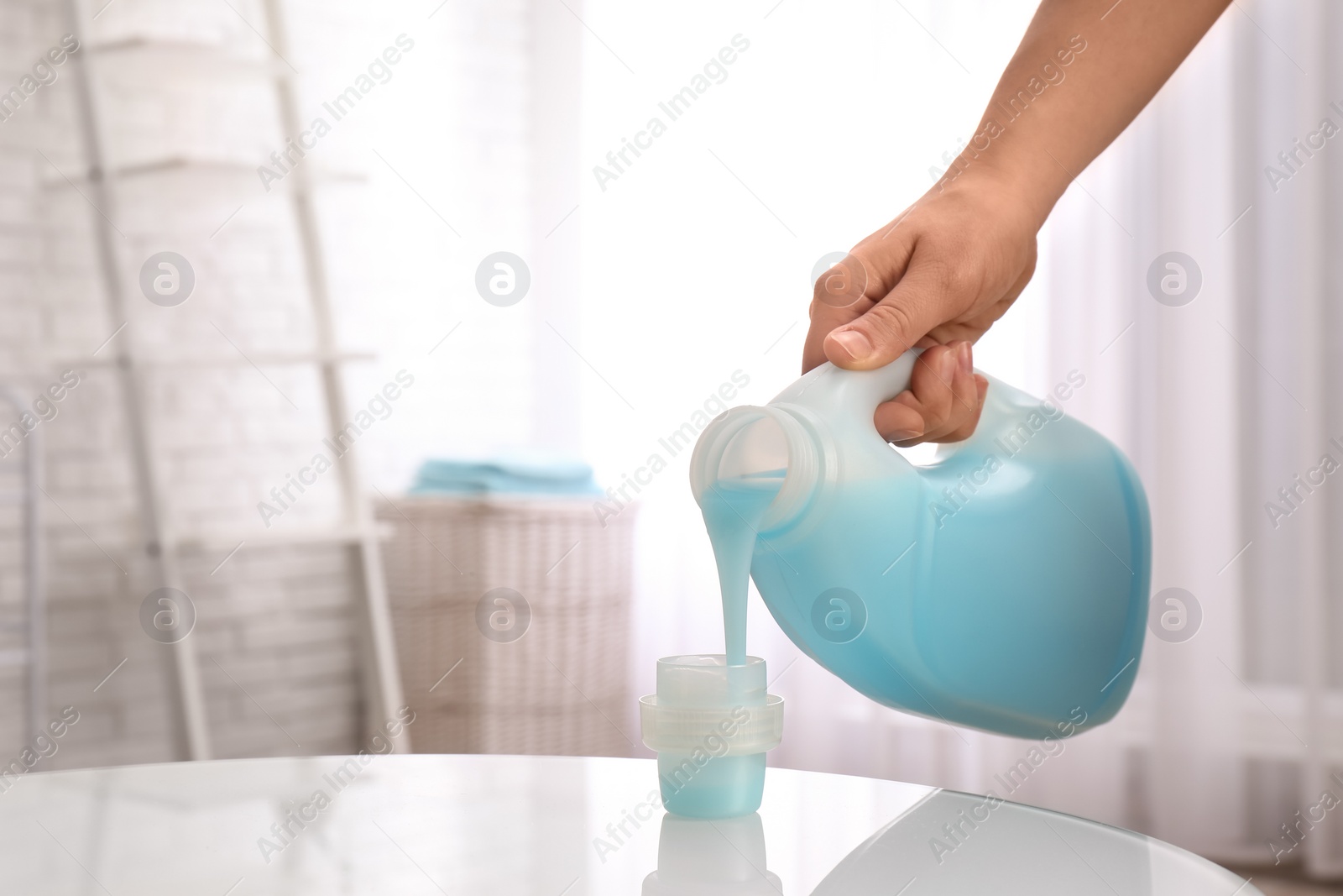 Photo of Woman pouring detergent into cap on table indoors, closeup with space for text. Laundry day