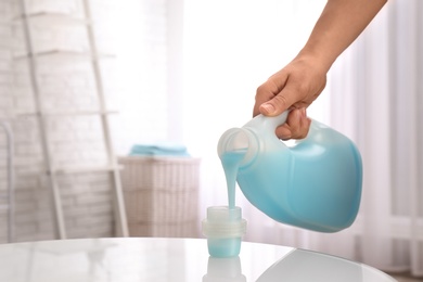 Woman pouring detergent into cap on table indoors, closeup with space for text. Laundry day