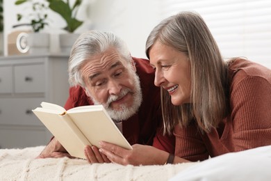 Photo of Lovely senior couple reading book on bed at home