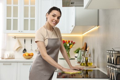 Photo of Woman cleaning electric cooktop with sponge wipe in kitchen