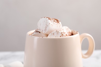 Photo of Cup of aromatic hot chocolate with marshmallows and cocoa powder on table against beige background, closeup