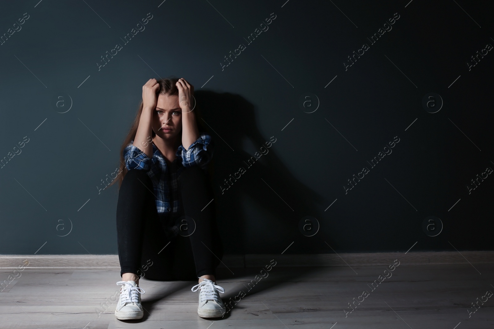 Photo of Depressed young woman sitting on floor in darkness