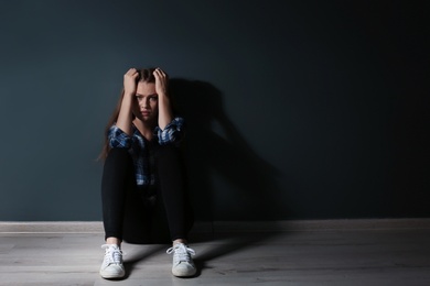 Photo of Depressed young woman sitting on floor in darkness